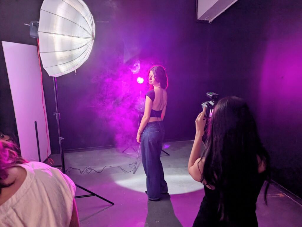 Étudiante prenant une photo d'un modèle dans un studio de l'ETPA lors d'un stage d'été, avec éclairage coloré et effets de fumée.